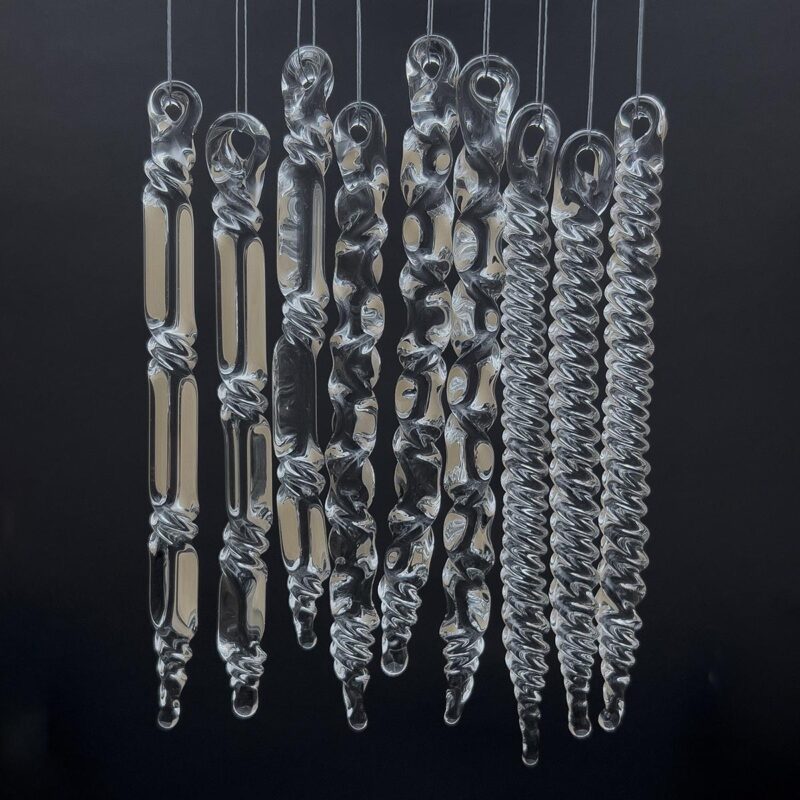 Assorted glass icicles with different twists hanging in front of a black background.