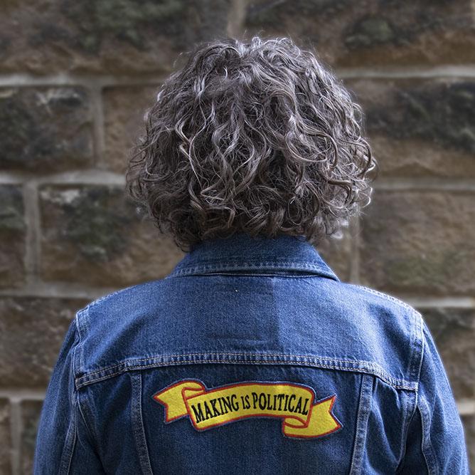 Joy facing away from the camera. She has brown curly hair and is wearing a denim jacket embroidered with the words MAKING IS POLITICAL