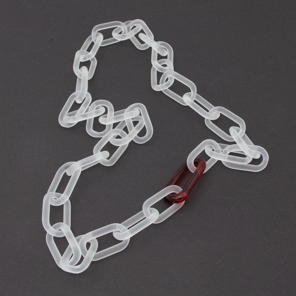 Glass chain necklace made with frosted links of clear glass and a single link of transparent red glass. The chain is arranged in a hear shape on a dark background.
