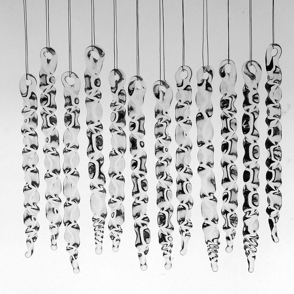 12 large clear glass icicles with hanging loop and zig zag design. The icicles hand in front of a pale grey background.