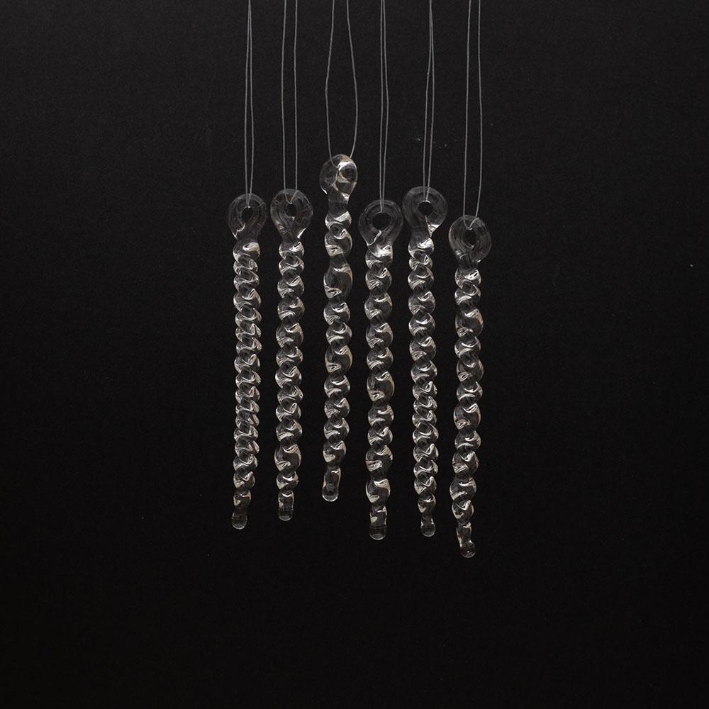 6 tiny clear glass icicles with hanging loop and twist design. The icicles hand in front of a black background.