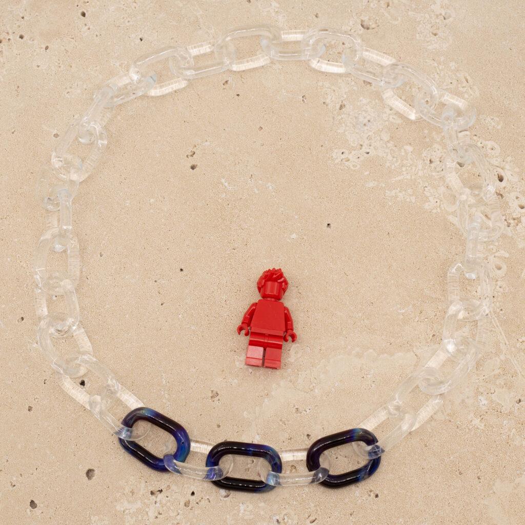 Clear and frosted link chain with three purple and blue Dragon Eye links sitting on a sandstone tile. Shown with a red lego figure for scale.