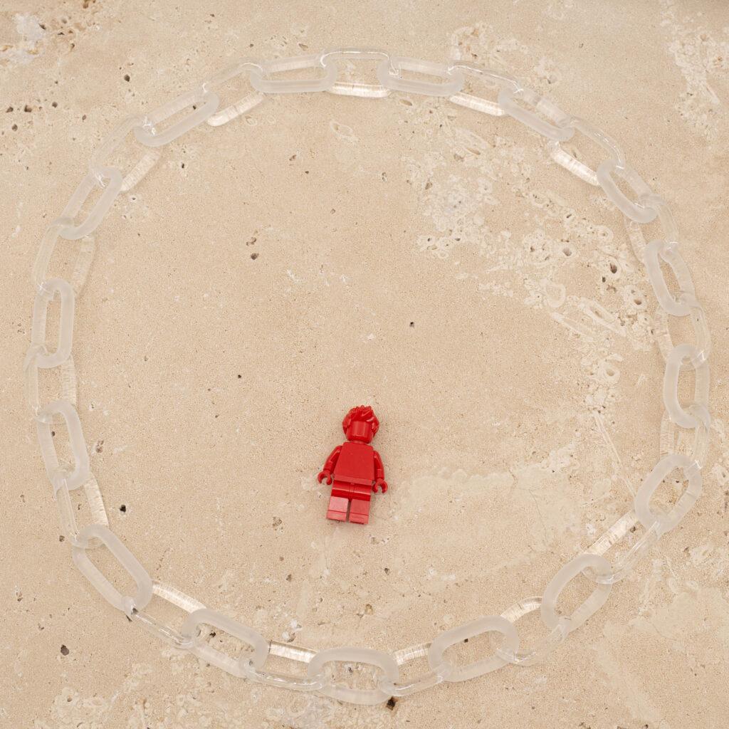 Alternating clear and frosted link chain sitting on a sandstone tile. Shown with a red lego figure for scale.