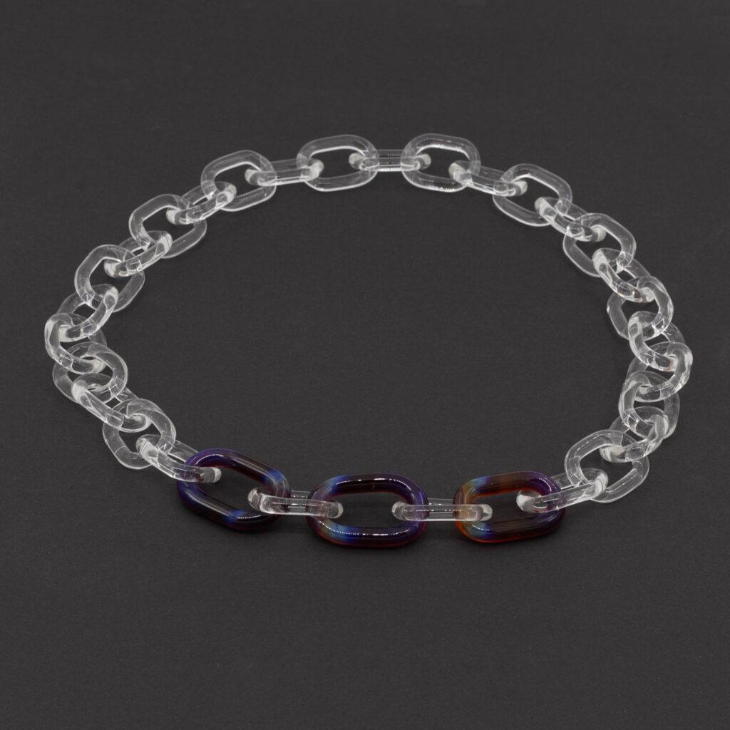 Clear glass link chain with three mai-tai links sitting on a dark background.
