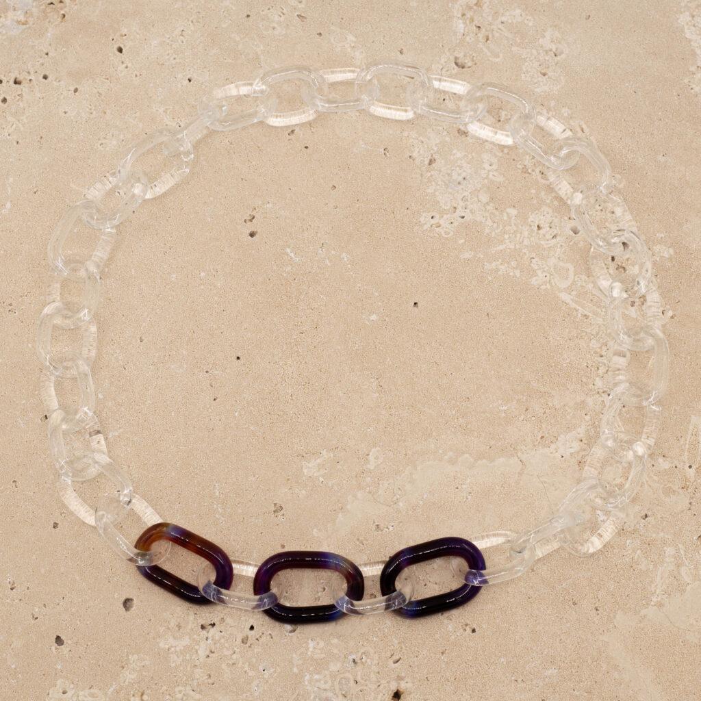 Clear glass link chain with three mai-tai links sitting on a sandstone tile.
