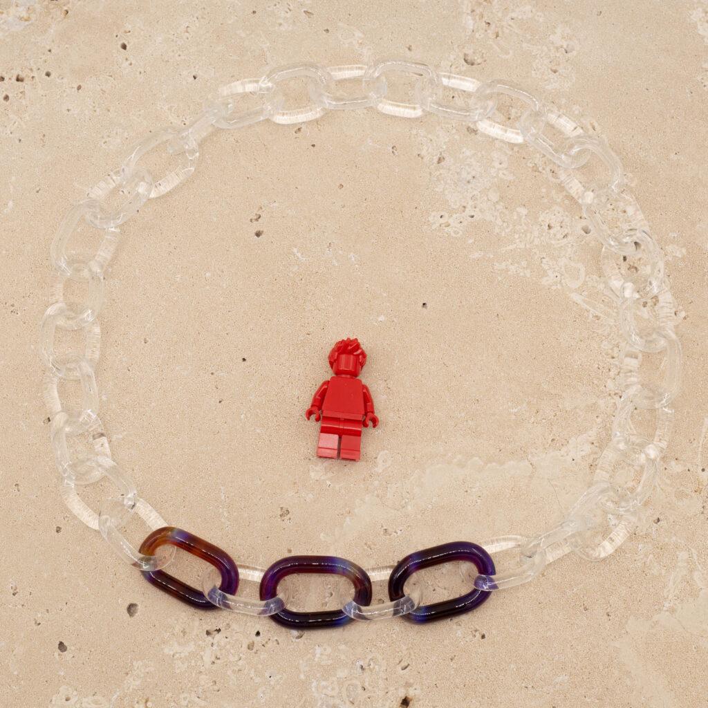 Clear glass link chain with three mai-tai links sitting on a sandstone tile. Shown with a red lego figure for scale.