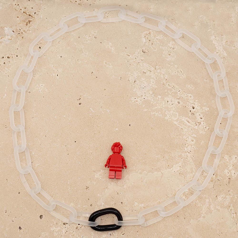 Frosted clear glass chain with a single black link sitting on a sandstone tile. Shown with a red lego figure for scale.