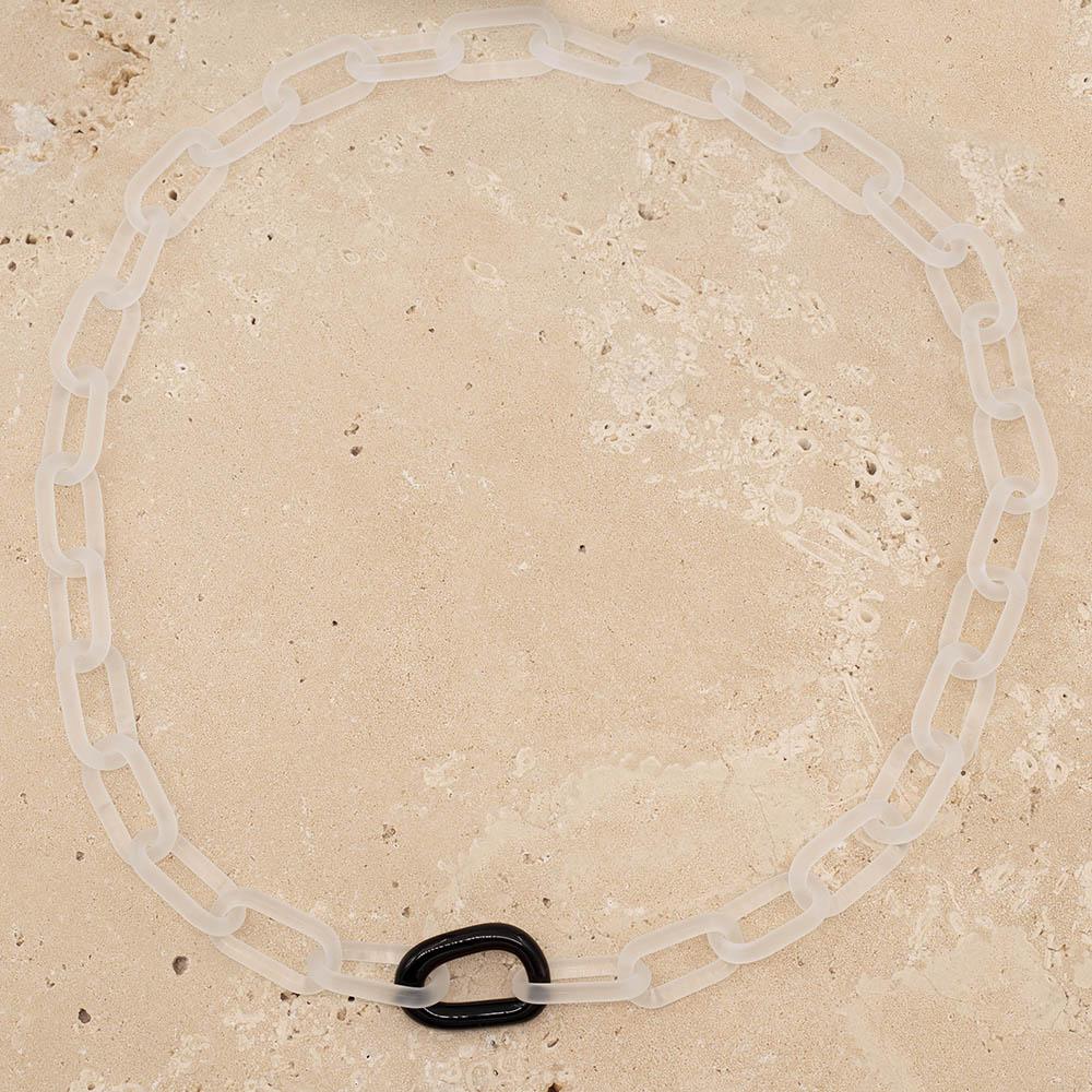 Frosted clear glass chain with a single black link sitting on a sandstone tile.
