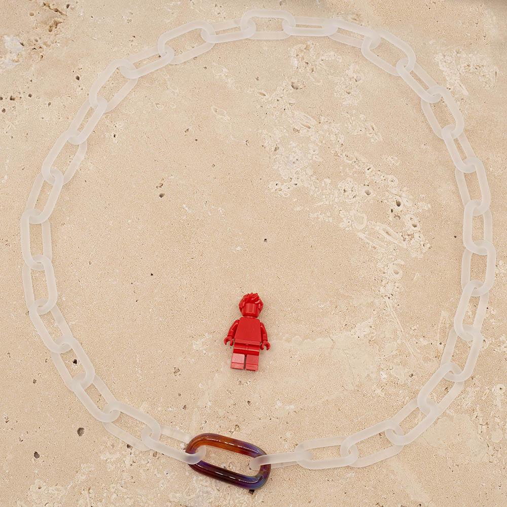 Frosted clear glass chain with multi colour link necklace sitting on a sandstone tile. Shown with a red lego figure for scale.