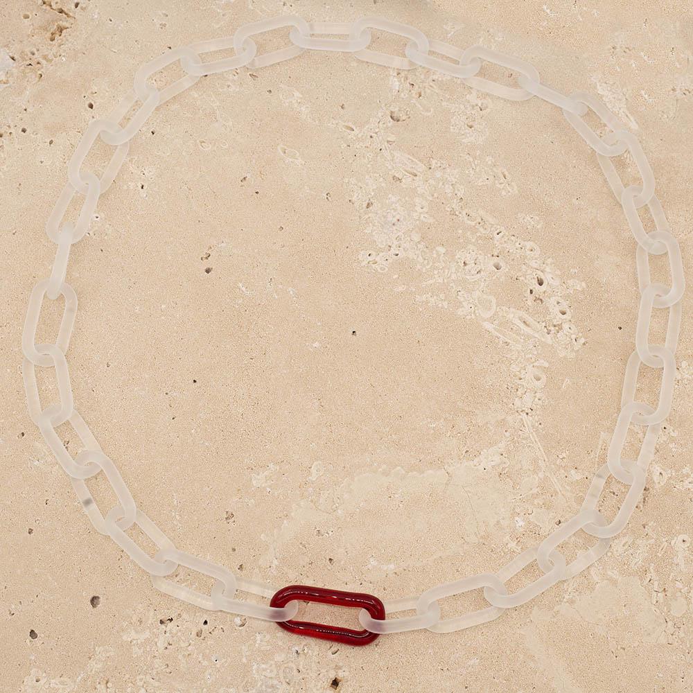 Frosted clear glass chain with single red link necklace sitting on a sandstone tile.