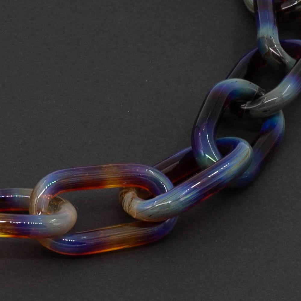 Close up of transparent multicolour glass chain link necklace on a dark background.