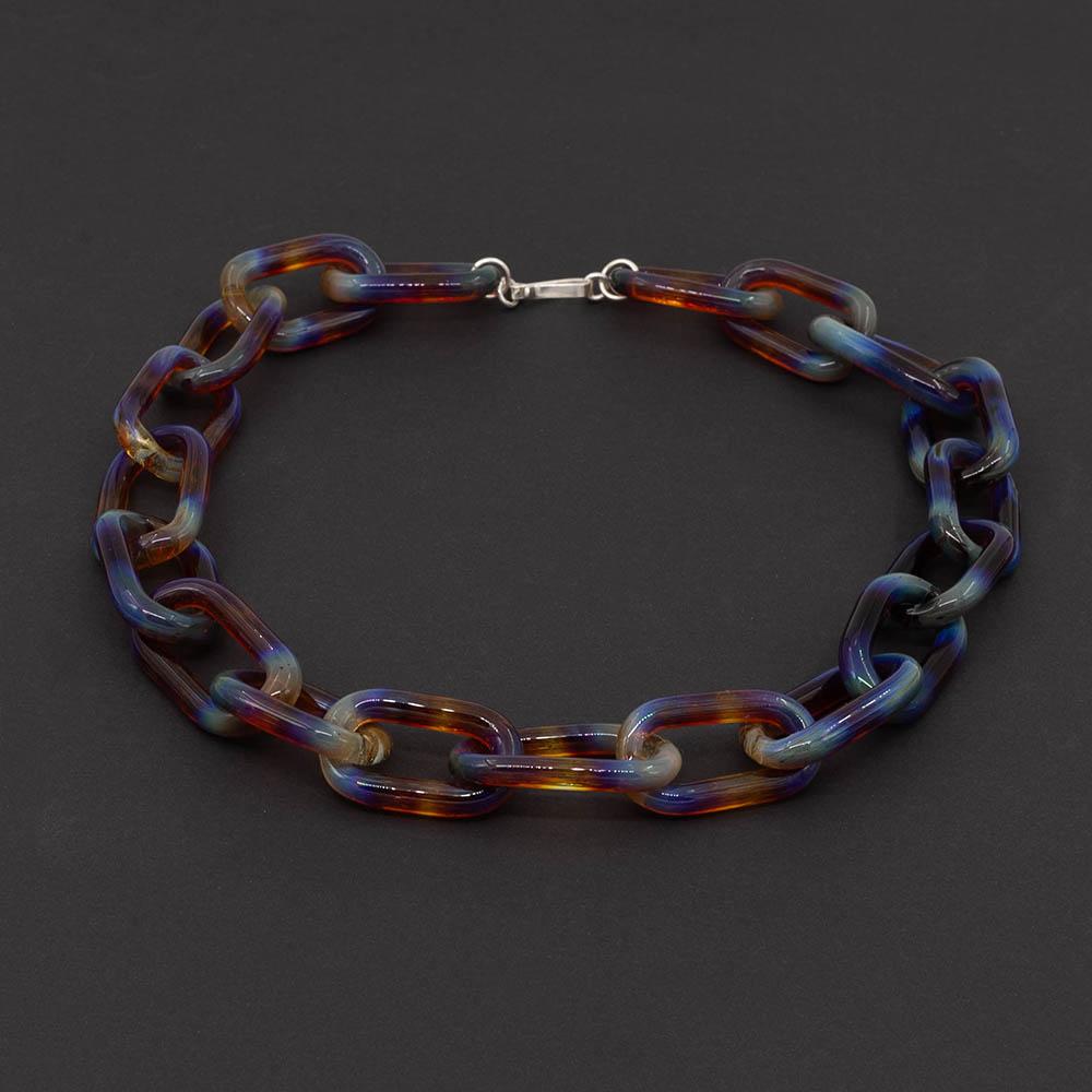 Transparent multicolour glass chain link necklace with a sterling silver hook and loop catch. Each link has blue, yellow, orange, purple and pink. The necklace sits on a dark background.