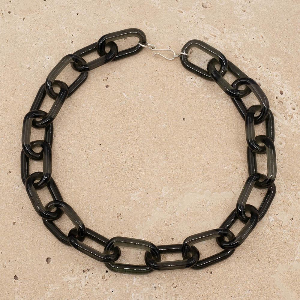 Transparent black glass chain link necklace with a sterling silver hook and loop catch. The necklace sits on a sandstone tile.