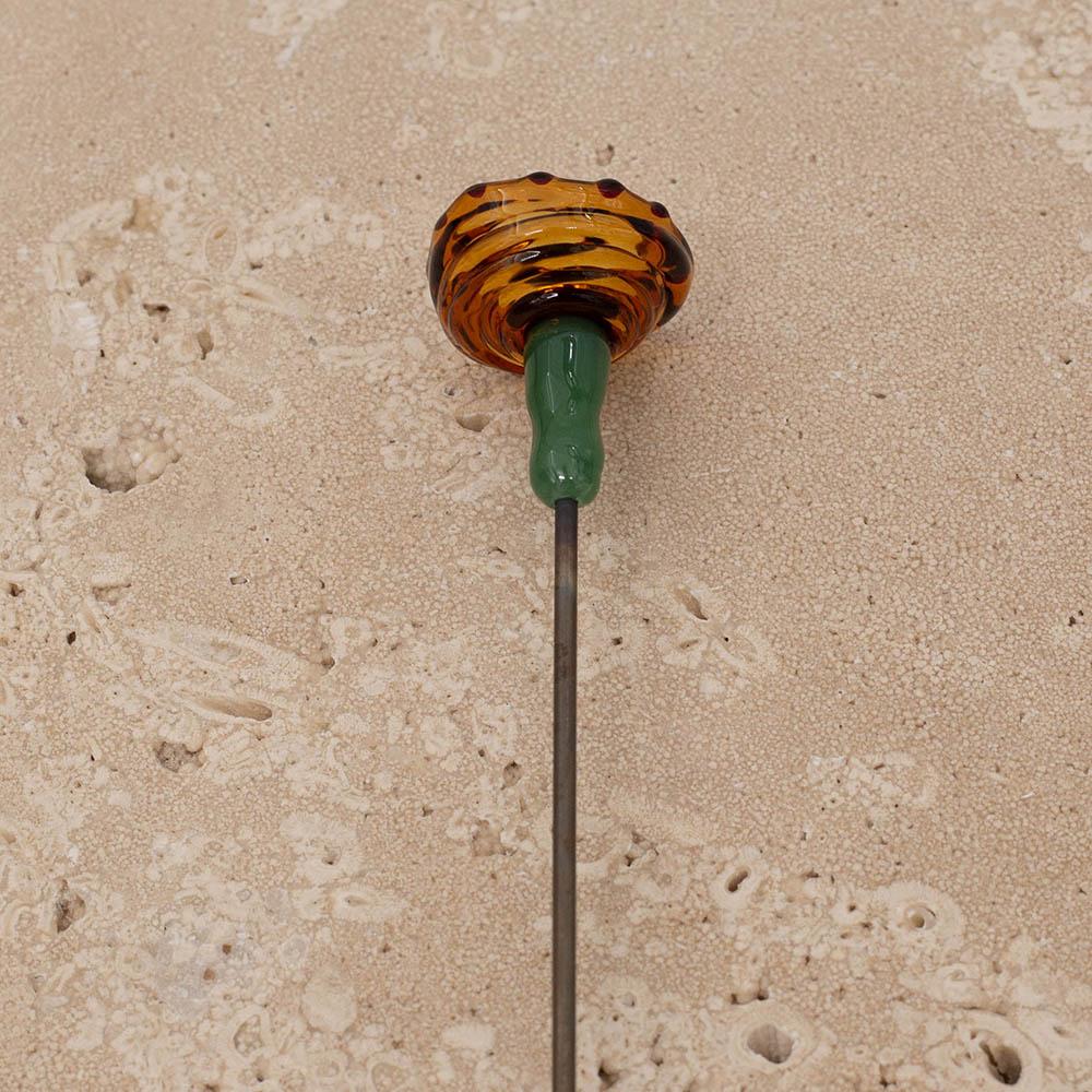 Back view of bee sipper cup in transparent amber with black dots and centre. The bee sipper has a green stem and is on a stainless steel rod.