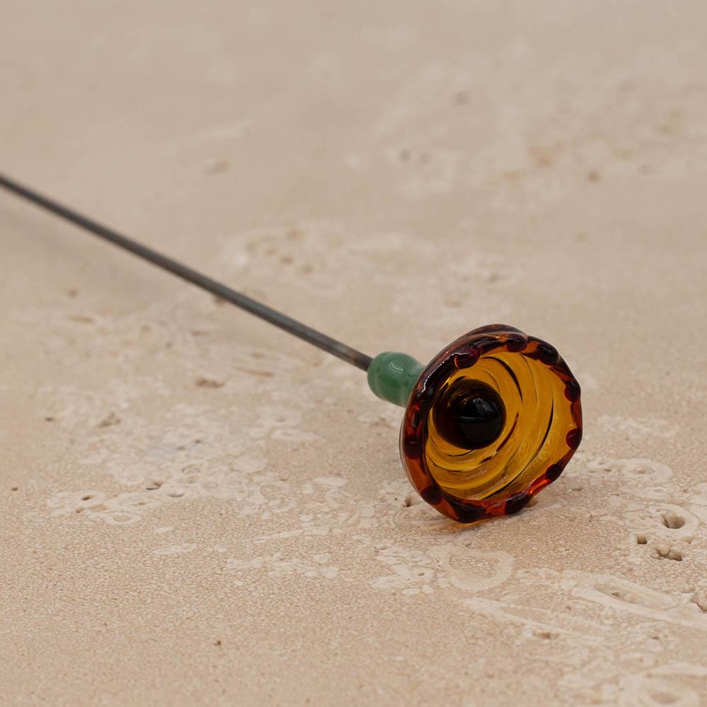 Bee sipper cup in transparent amber with black dots and centre. The bee sipper has a green stem and is on a stainless steel rod.