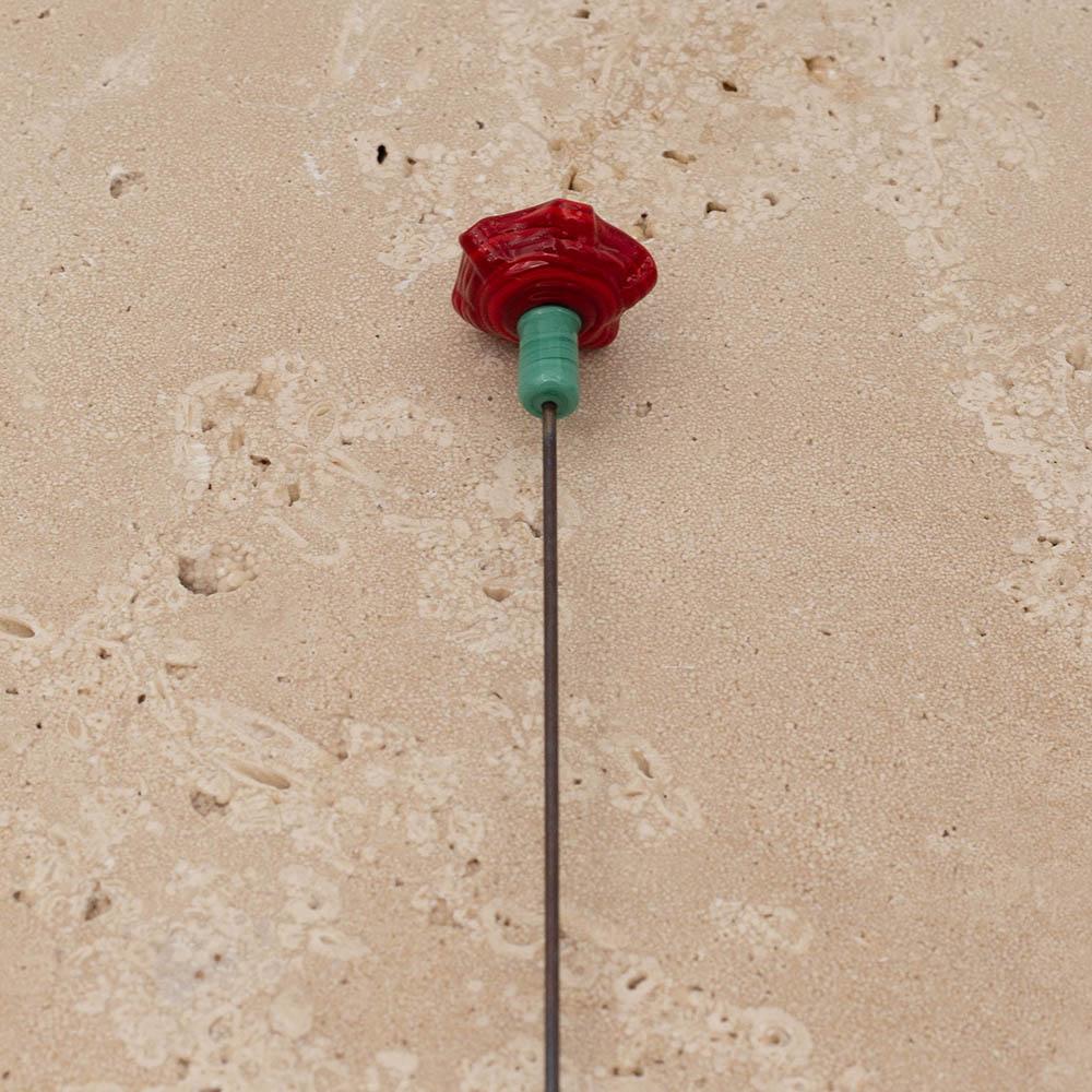 Back view of red ruffled glass bee sipper with black centre and green stem.