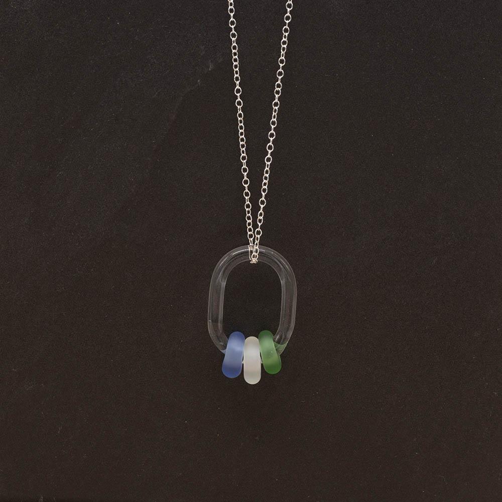 A clear glass link which passes through 3 frosted beads made from green, clear and blue glass. The link hangs from a silver chain. Shown on a slate background.