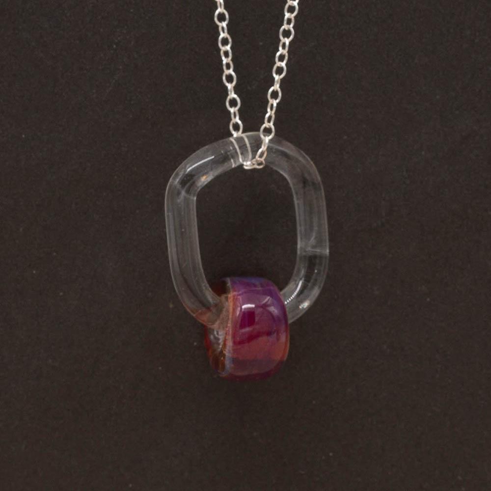 Close up of a clear glass link which passes through a barrel shaped bead made with pink mai tai glass. The link hangs from a silver chain. Shown on a slate background.
