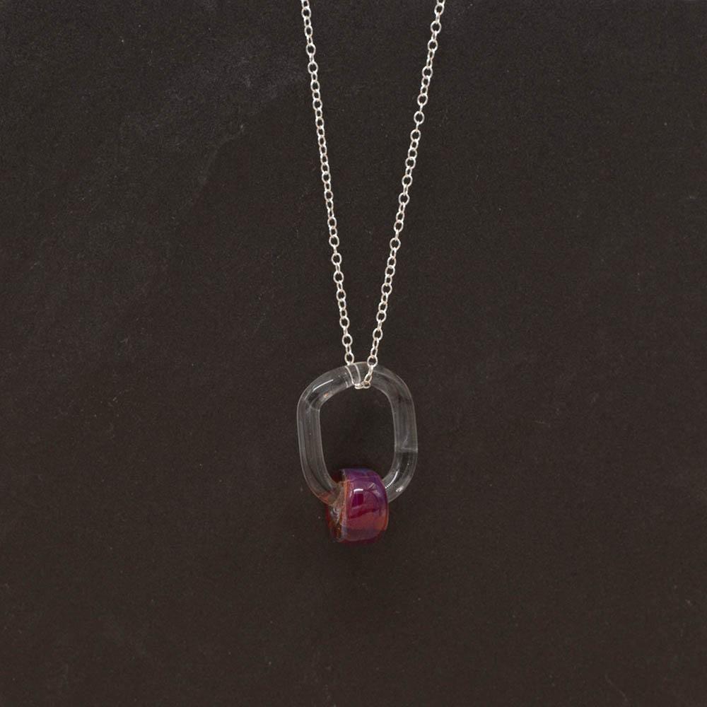 A clear glass link which passes through a barrel shaped bead made with pink mai tai glass. The link hangs from a silver chain. Shown on a slate background.