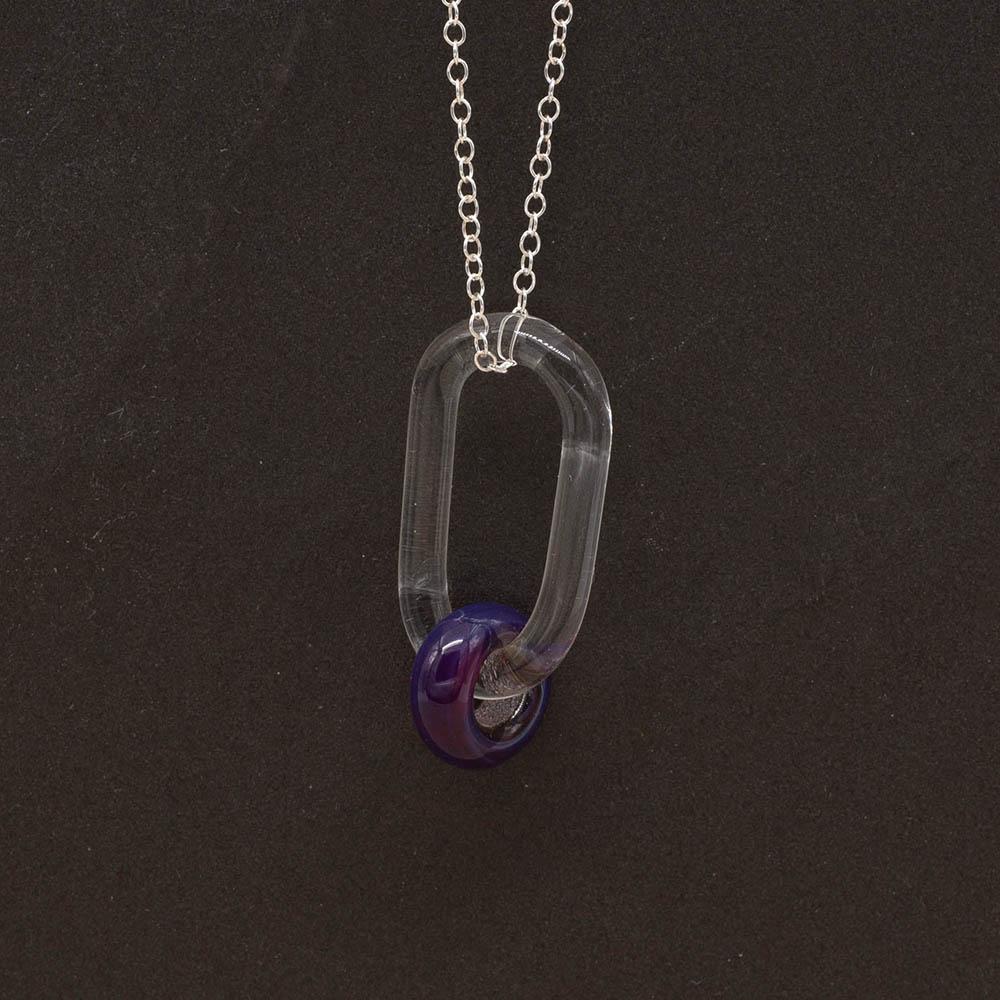 Close up of a clear glass link which passes through a bead made with purple and blue mai tai glass. The link hangs from a silver chain. Shown on a slate background.