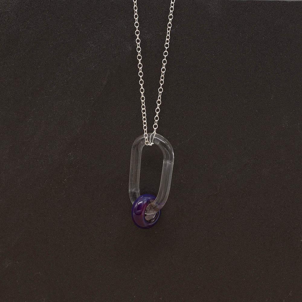A clear glass link which passes through a bead made with purple and blue mai tai glass. The link hangs from a silver chain. Shown on a slate background.