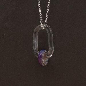 Close up of a clear glass link which passes through a bead made from purple glass. The link hangs from a silver chain. Shown on a slate background.