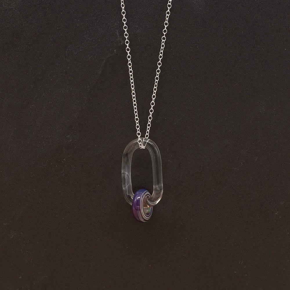 A clear glass link which passes through a bead made from purple glass. The link hangs from a silver chain. Shown on a slate background.