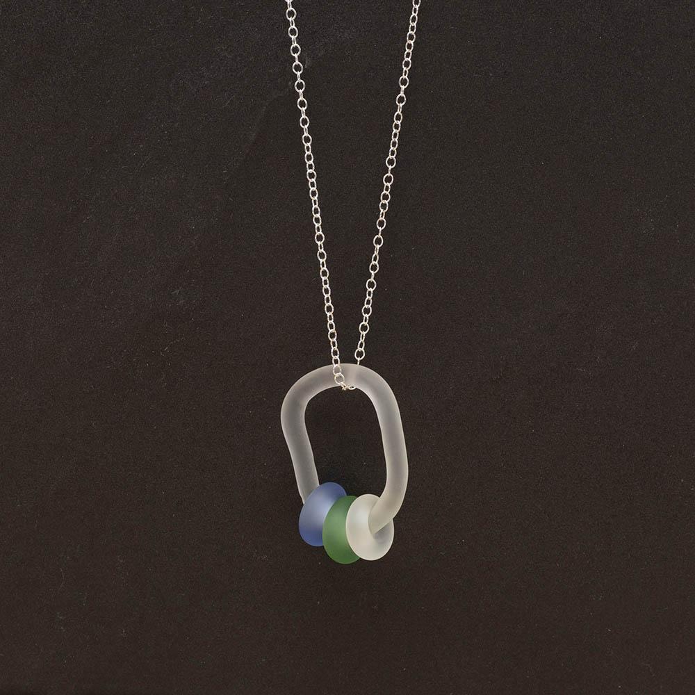 A frosted glass link which passes through 3 beads made from green, clear and blue glass. The link hangs from a silver chain. Shown on a slate background.