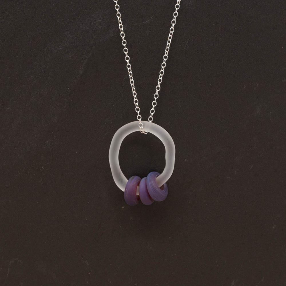 A frosted glass link which passes through 3 frosted blueberry coloured beads. The link hangs from a silver chain. Shown on a slate background.