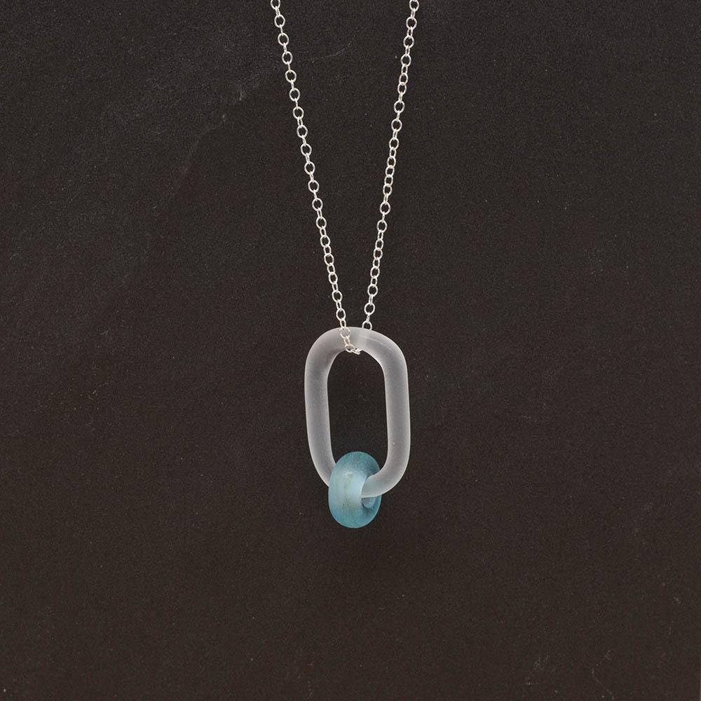 A frosted glass link which passes through a bead made from a turquoise Bombay Sapphire gin bottle. The link hangs from a silver chain. Shown on a slate background.