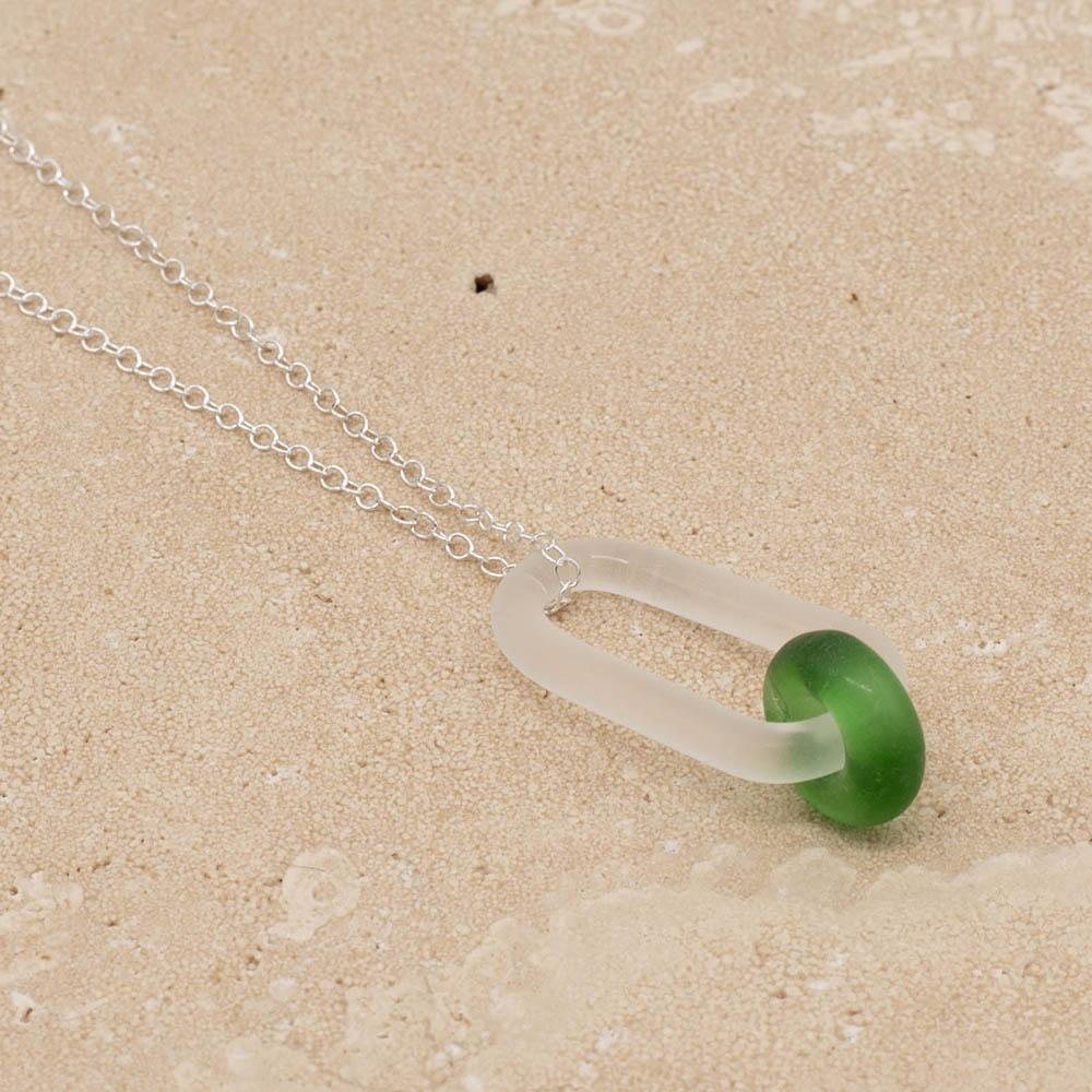 Close up of a frosted glass link which passes through a bead made from a green Gordons gin bottle. The link hangs from a silver chain. Shown on a sandstone background.