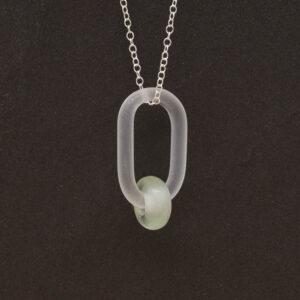 Close up of frosted glass link which passes through a bead made from pale green wine bottle glass. The link hangs from a silver chain. Slate background.