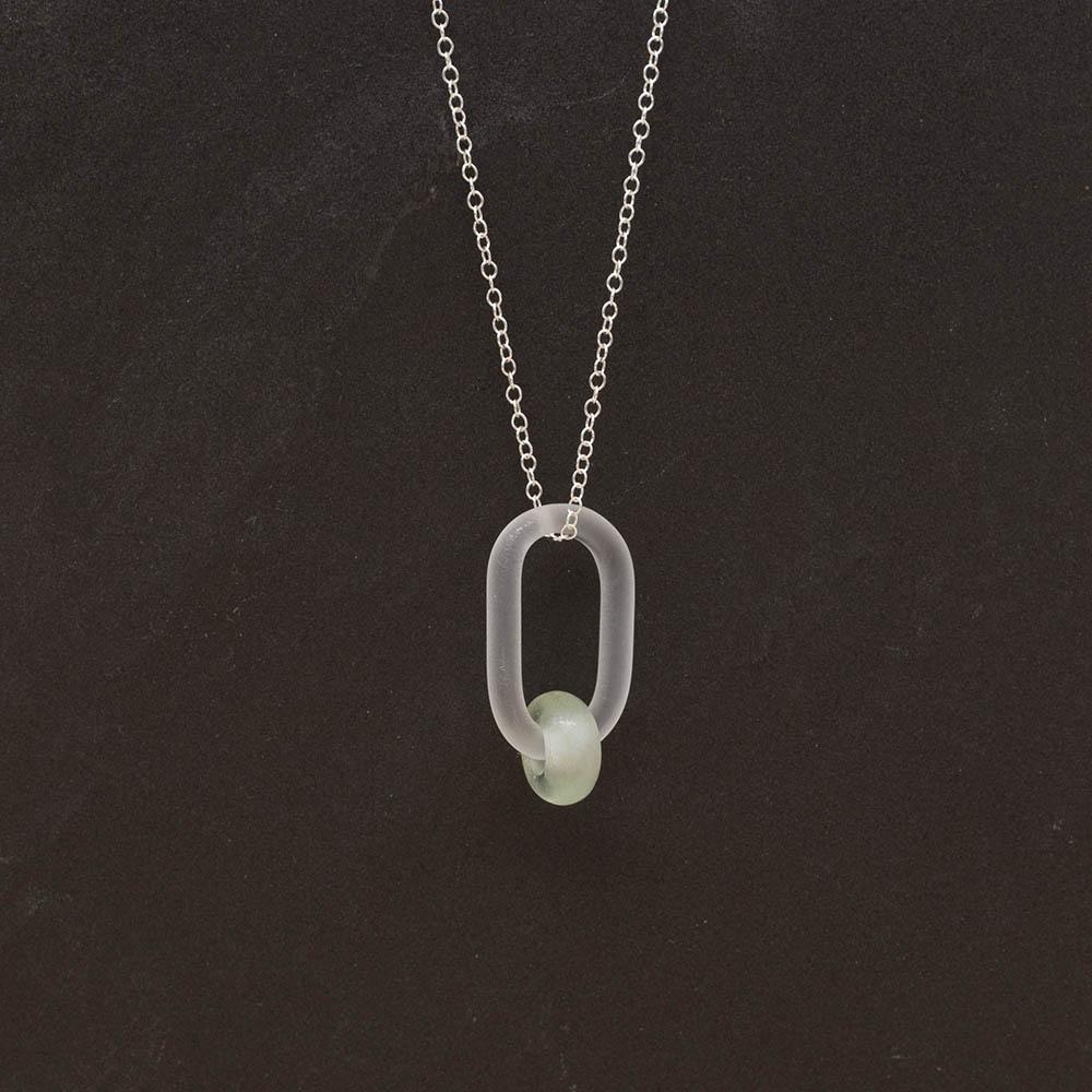Frosted glass link which passes through a bead made from pale green wine bottle glass. The link hangs from a silver chain. Slate background.