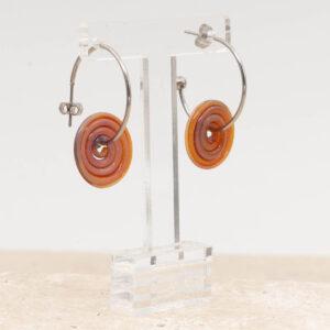 Side view of amber-purple glass disc hanging on a stainless steel hoop earring with a butterfly back.