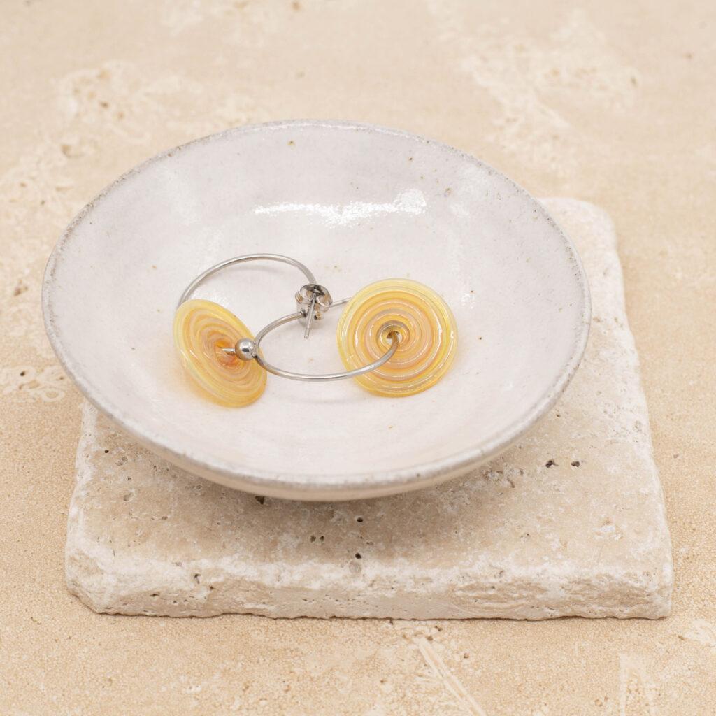 A pair of hoop earrings with orange yellow glass discs sitting in a small white bowl.
