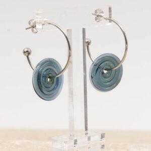 Side view of ocean blue glass disc hanging on a stainless steel hoop earring with a butterfly back.