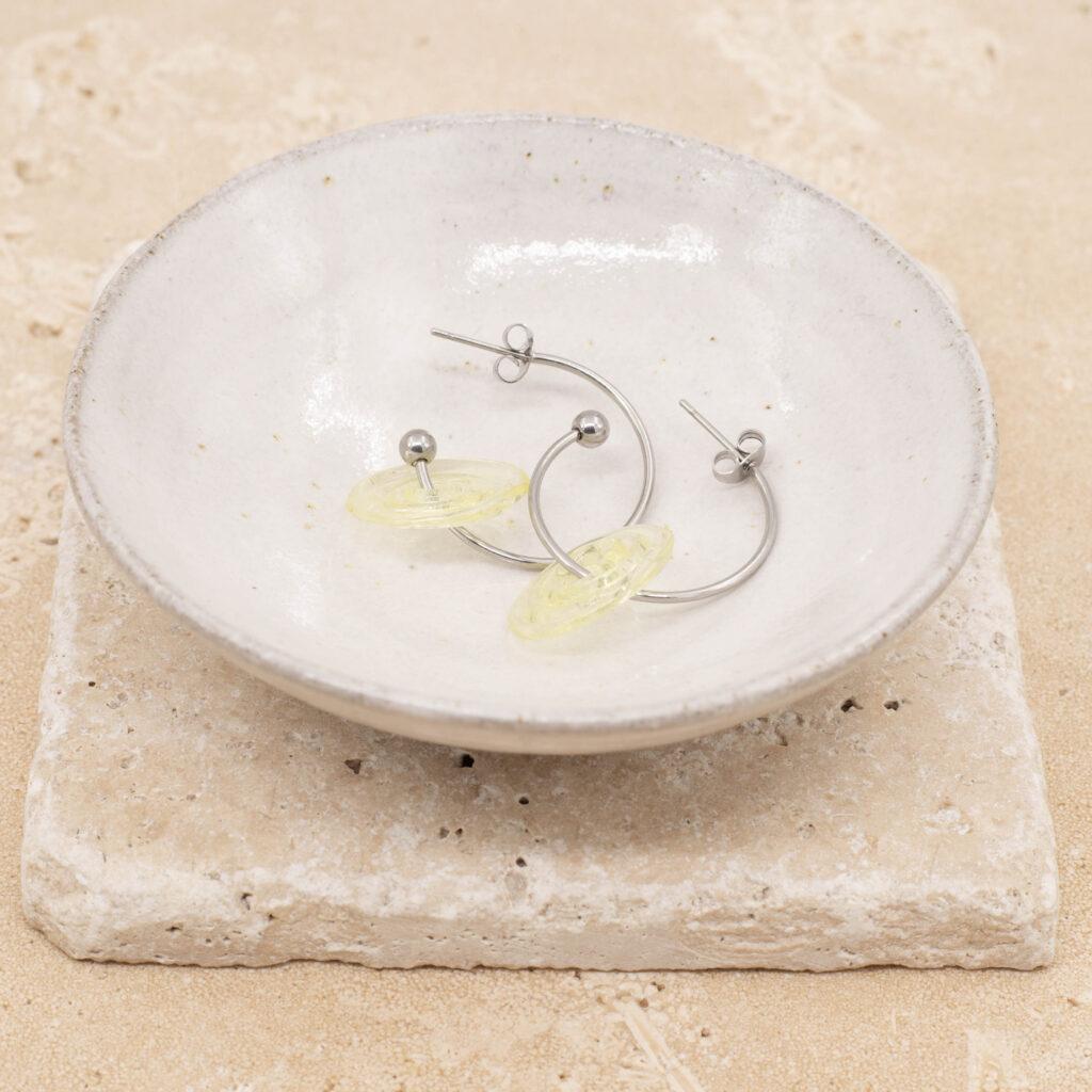 A pair of hoop earrings with pale yellow glass discs sitting in a small white bowl.