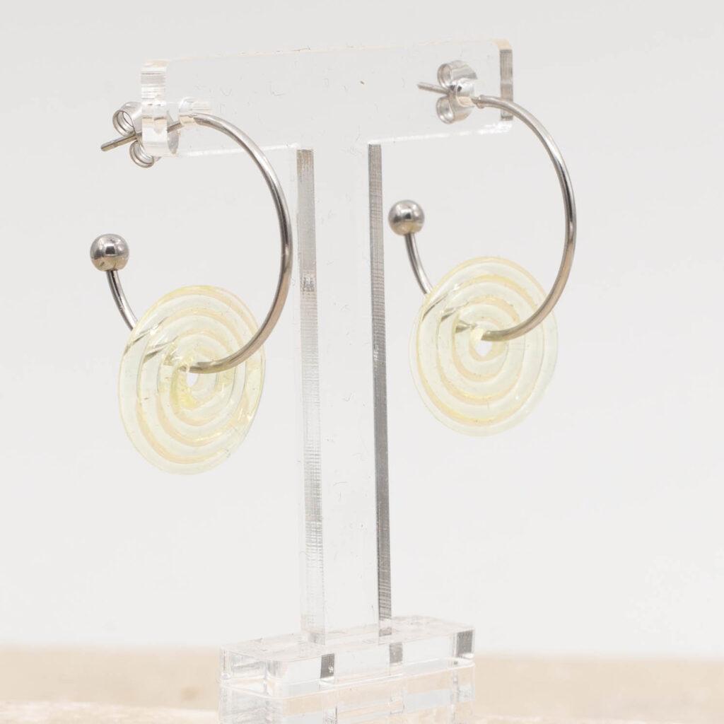 Side view of pale yellow glass disc hanging on a stainless steel hoop earring with a butterfly back.