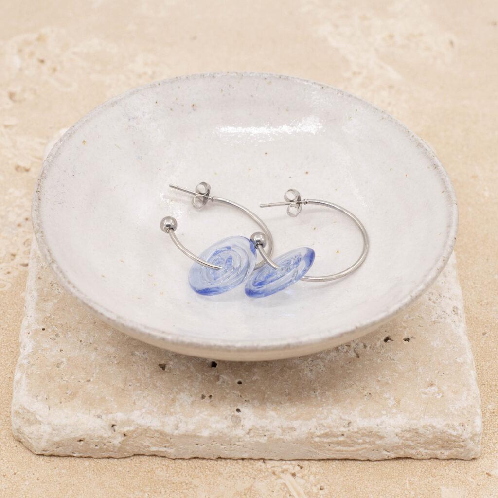 A pair of hoop earrings with pale blue glass discs sitting in a small white bowl.