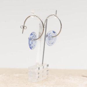 Side view of pale transparent blue glass disc hanging on a stainless steel hoop earring with a butterfly back.