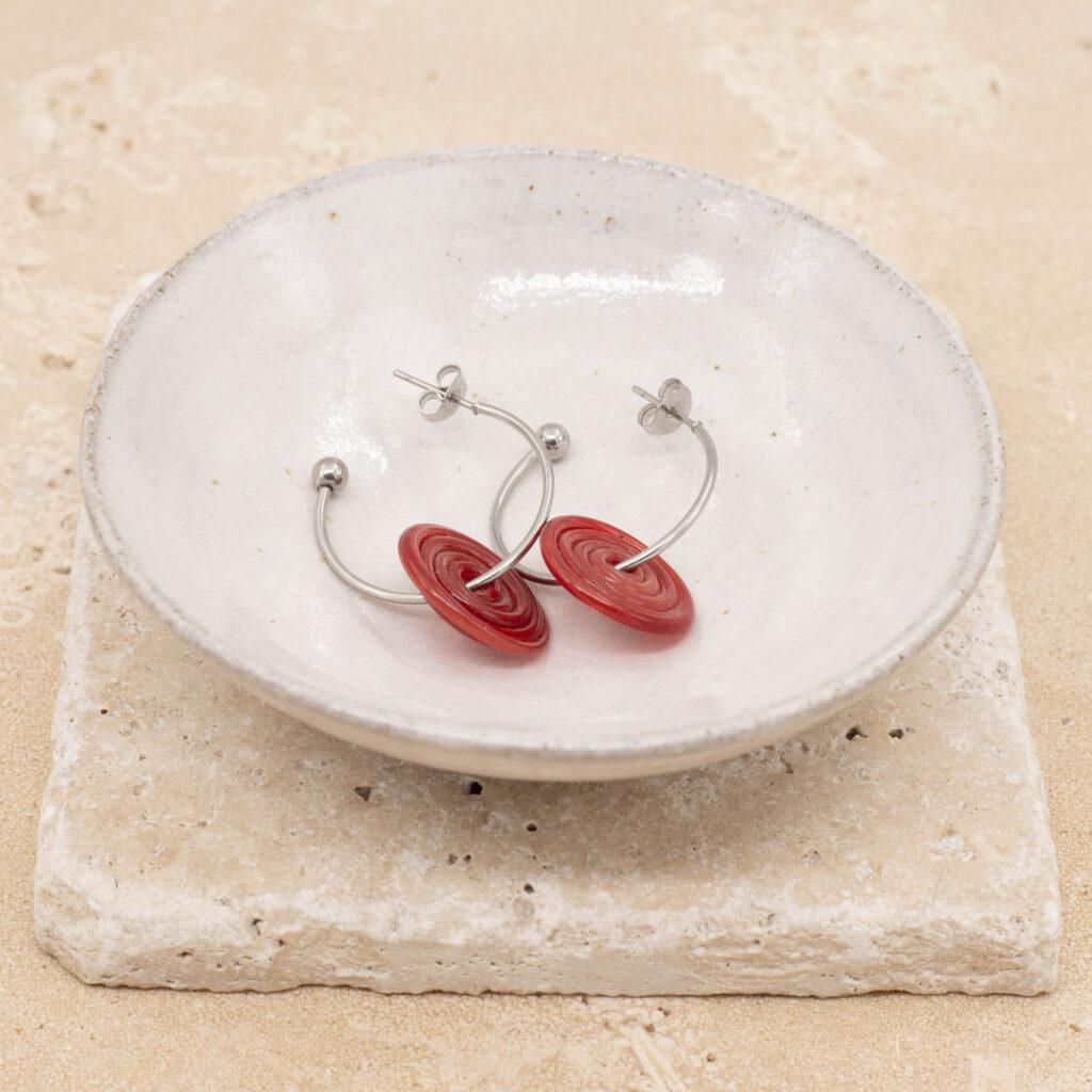 A pair of hoop earrings with red glass discs sitting in a small white bowl.