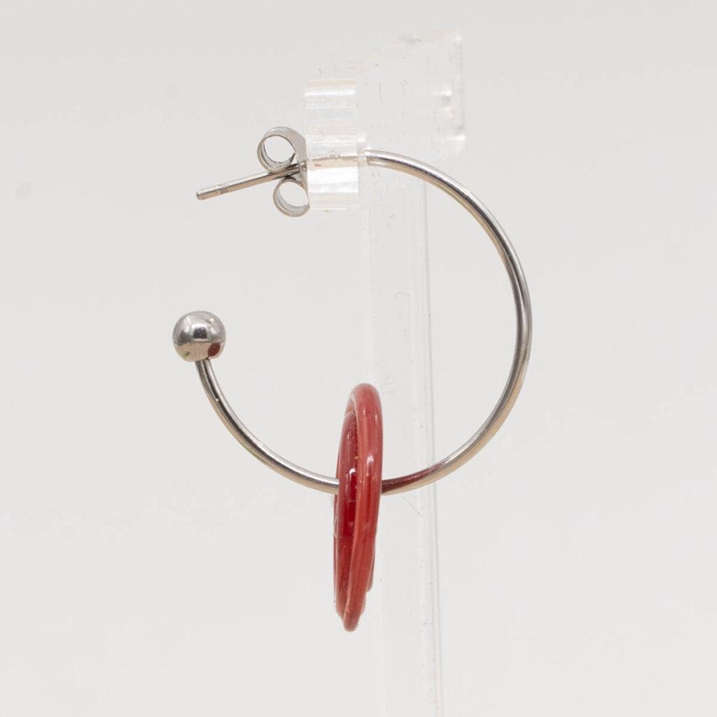 Side view of red glass disc hanging on a stainless steel hoop earring with a butterfly back.