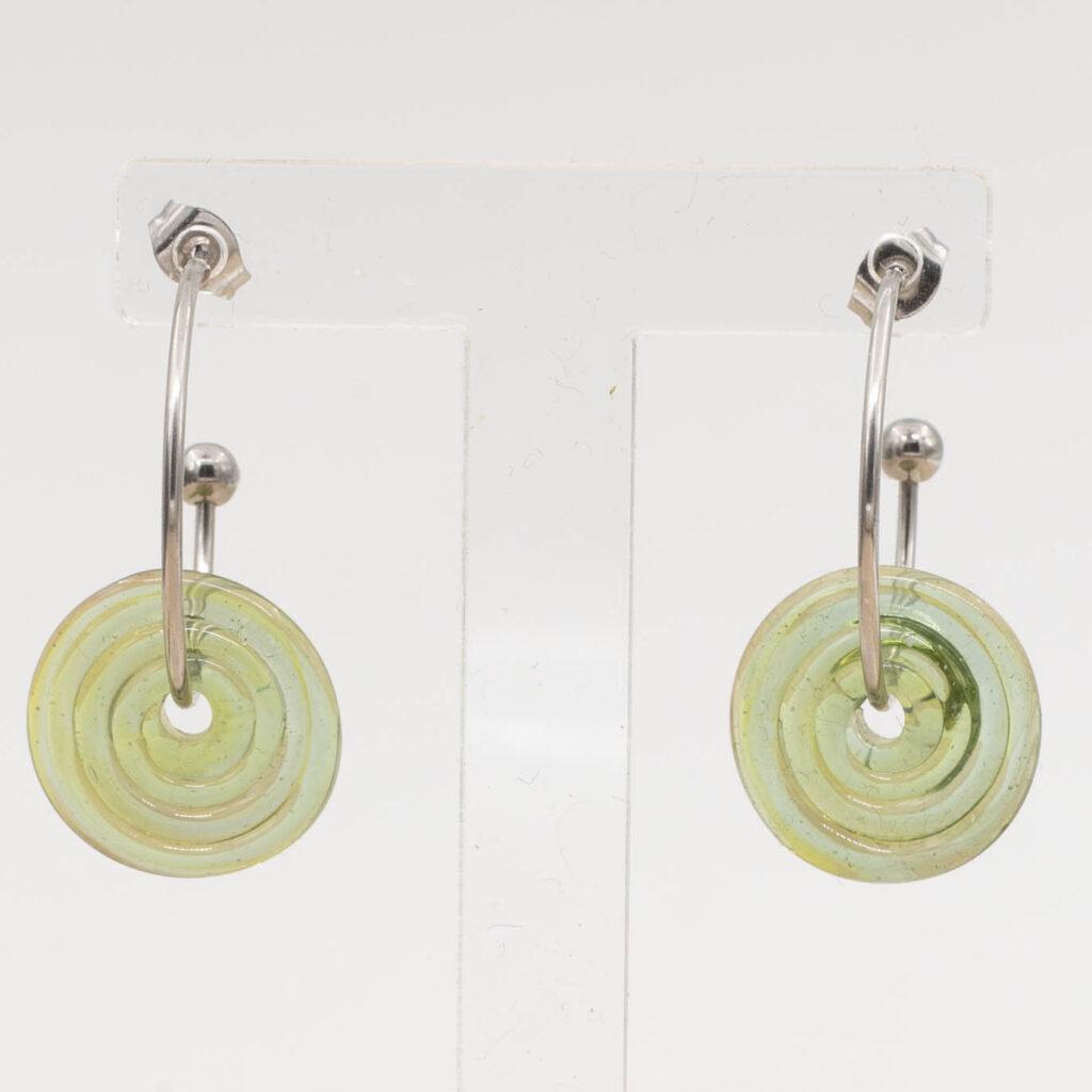 Close up of transparent green glass disc hanging on a stainless steel hoop earring with a butterfly back.