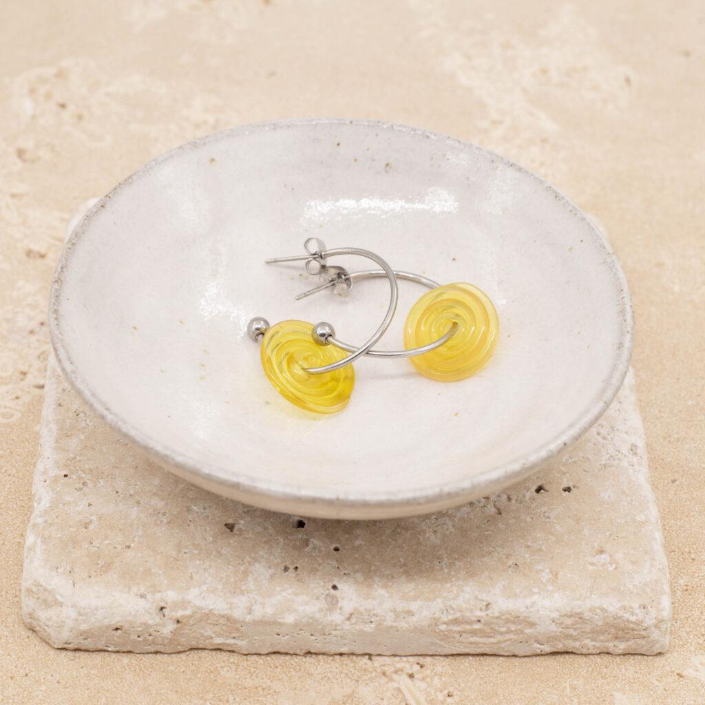 A pair of hoop earrings with sunshine yellow glass discs sitting in a small white bowl.