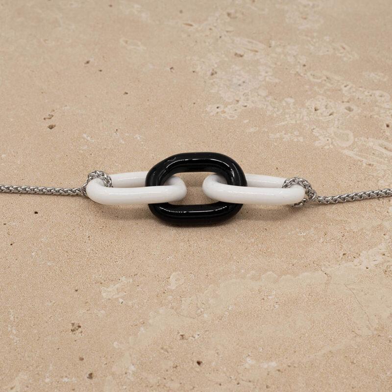 Close up of necklace with three alternating white and black glass links. The links are fastened to a chain to make a necklace. Shown on a sandstone background.