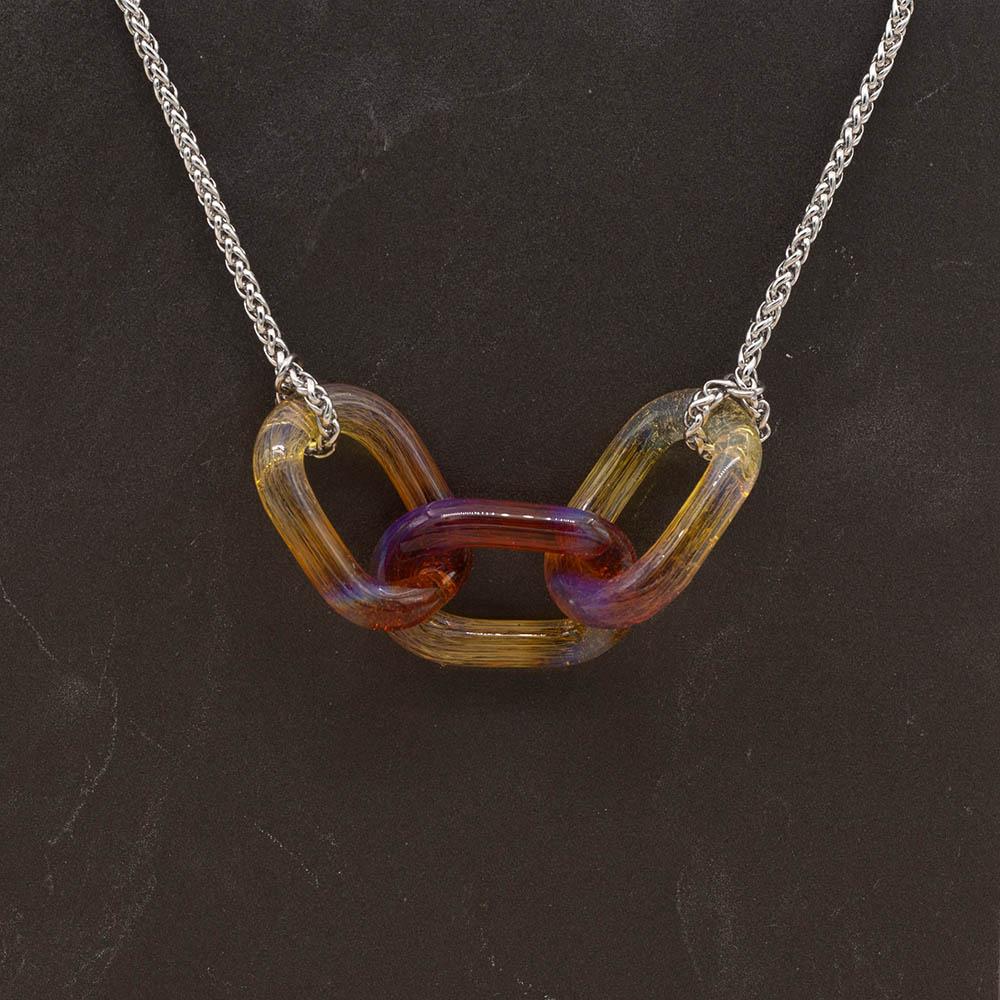 Necklace with three pink, orange and yellow glass links. The links are fastened to a chain to make a necklace. Shown on a slate background.