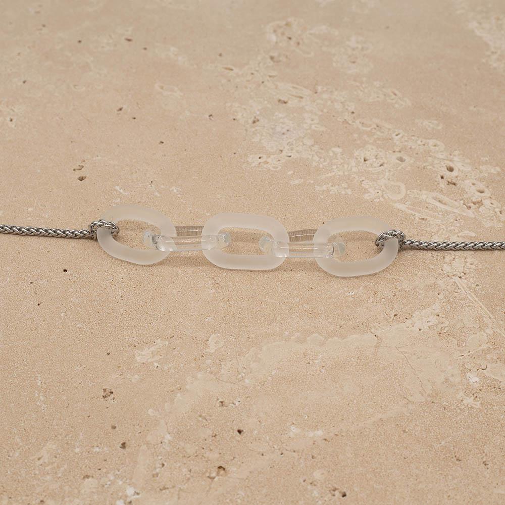 Close up of necklace with five alternating frosted and clear glass links. The links are fastened to a chain to make a necklace. Shown on a sandstone background.