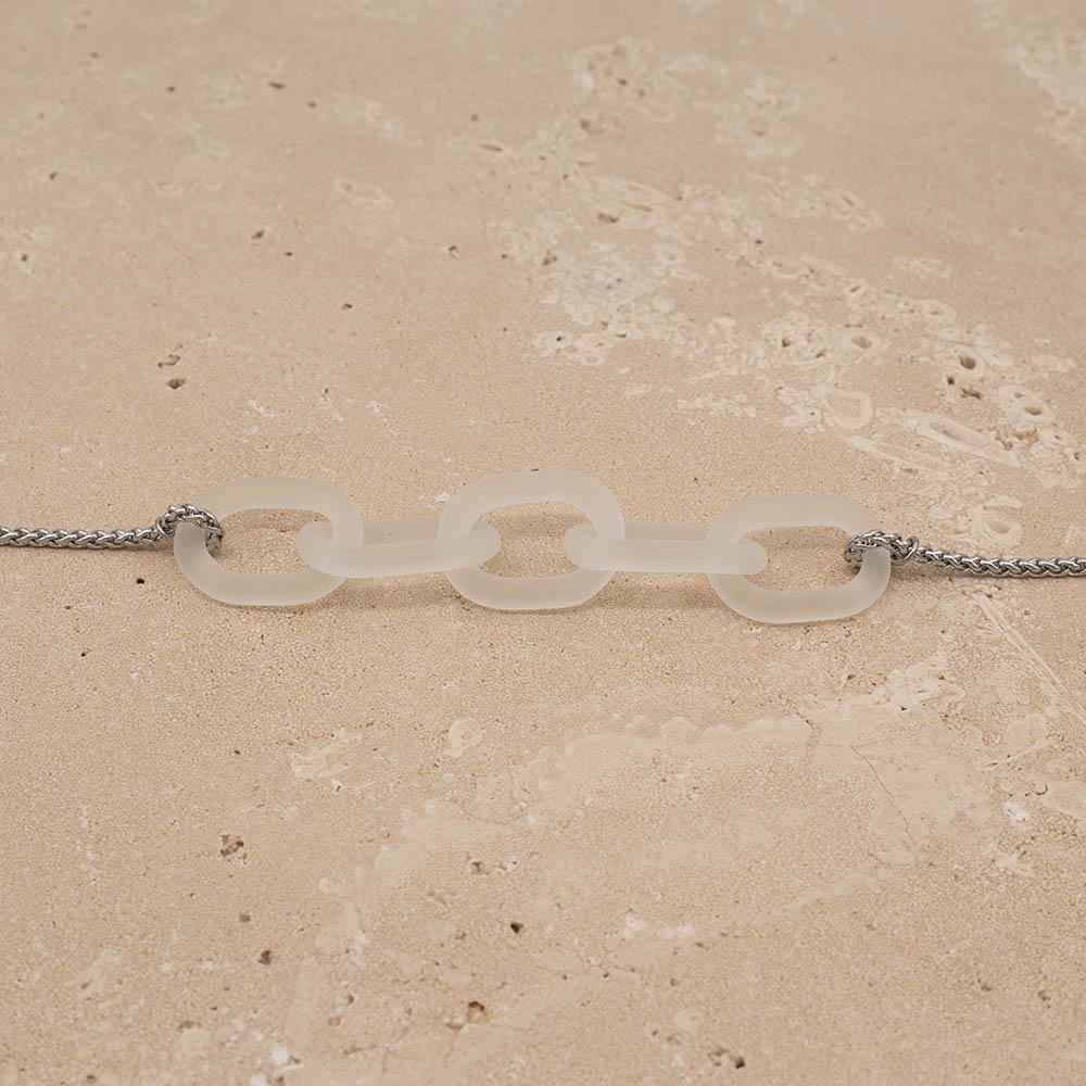 Close up of necklace with five frosted clear glass links. The links are fastened to a chain to make a necklace. Shown on a sandstone background.