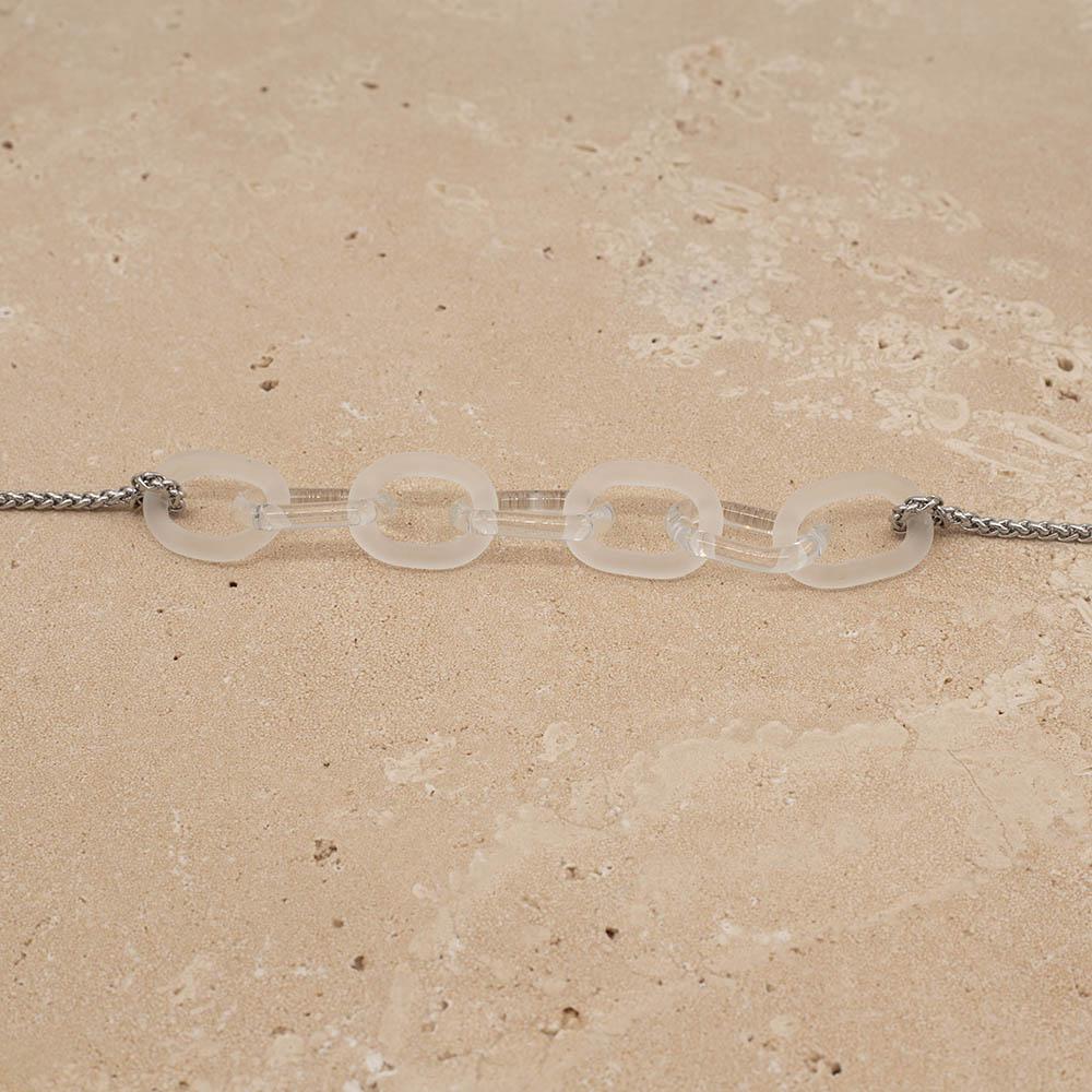 Close up of necklace with seven alternating frosted and clear glass links. The links are fastened to a chain to make a necklace. Shown on a sandstone background.