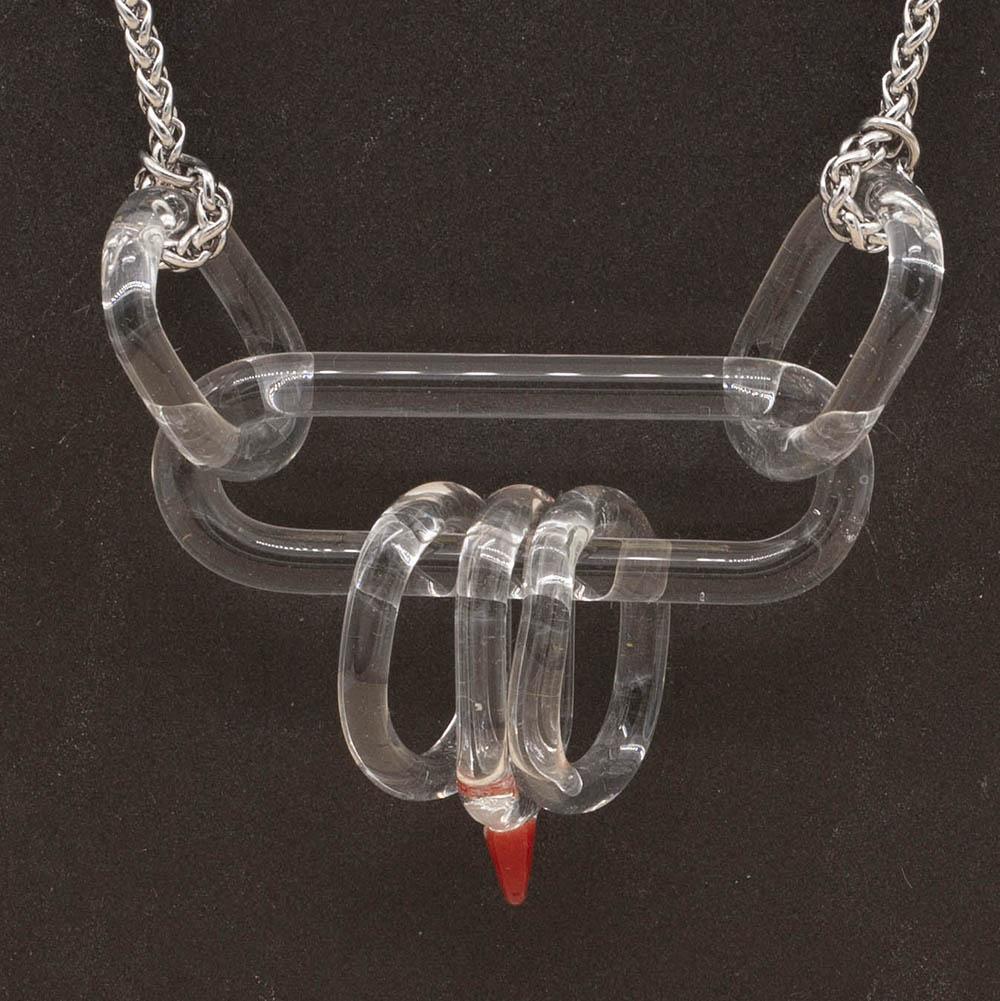 Close up of necklace with long clear glass link and five smaller clear links. One smaller link has a red accent. Shown on a slate background.